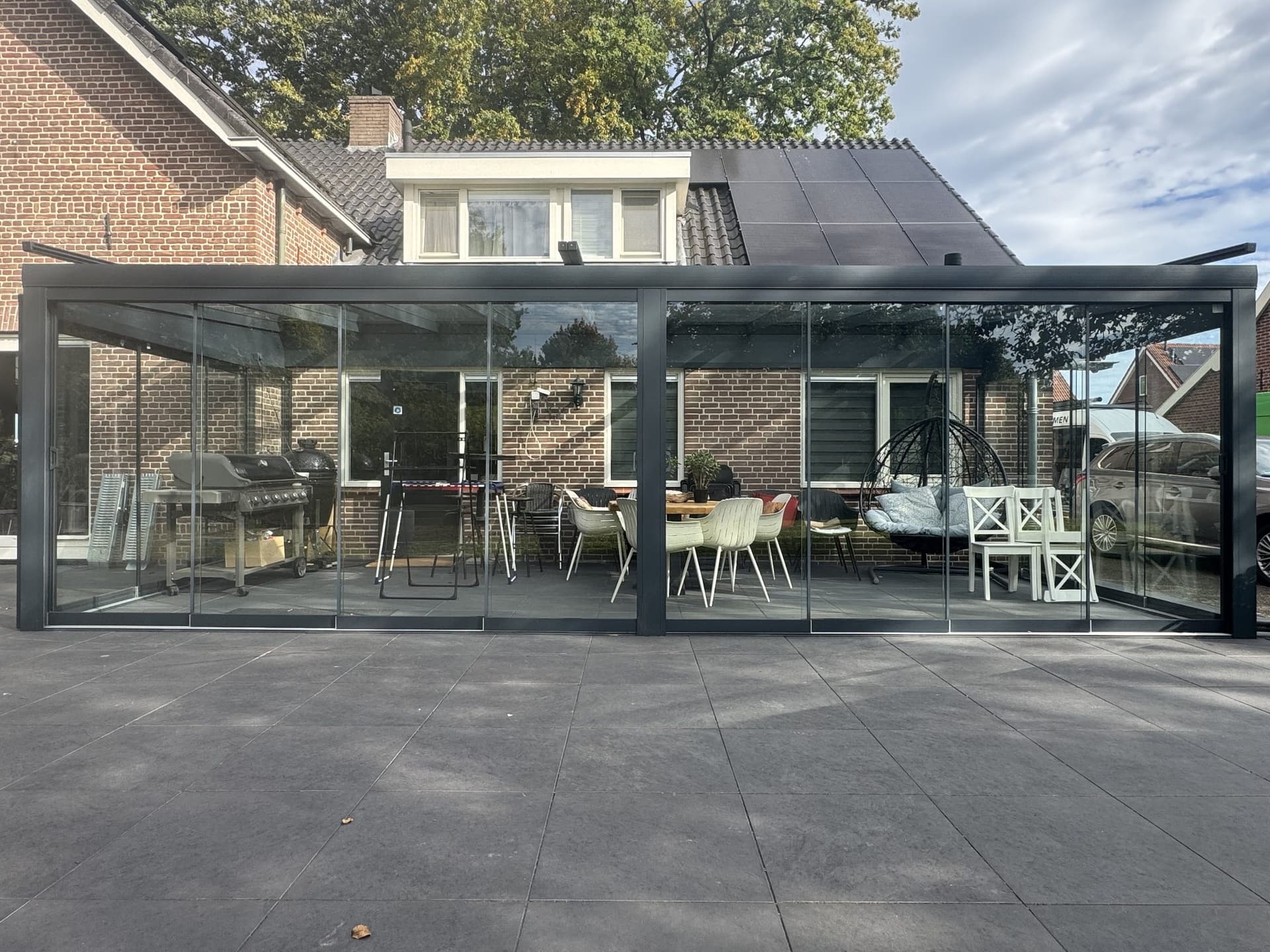 Tuinkamer met glazen dak en glazen schuifwanden tegen een bakstenen woning in Almelo, recht van voren